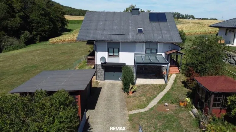 Luftaufnahme des Einfamilienhauses mit Carport, Garage und umliegender grüner Landschaft.