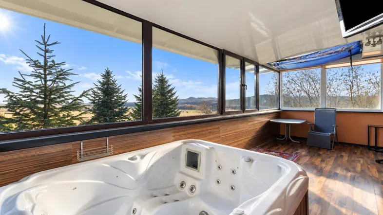 Heller Wintergarten mit Whirlpool und weitem Blick über die grüne Landschaft.