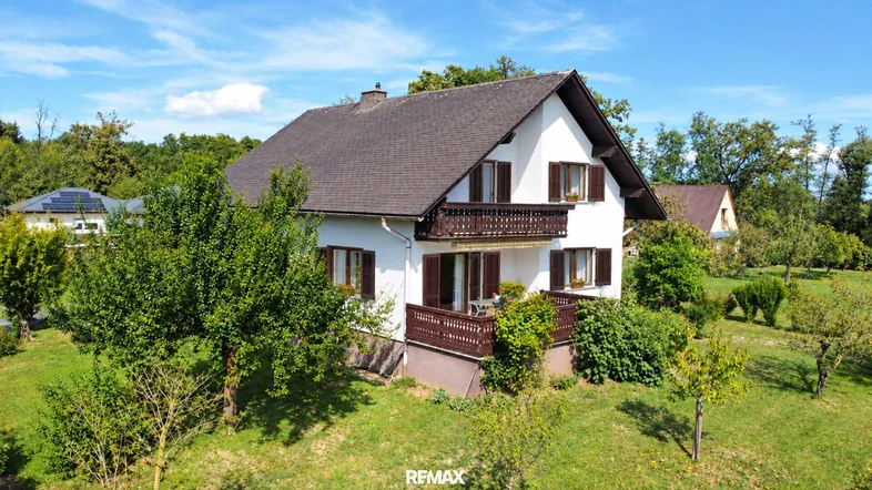 Freistehendes Einfamilienhaus mit Satteldach und Balkonen, umgeben von viel Grün und Bäumen.