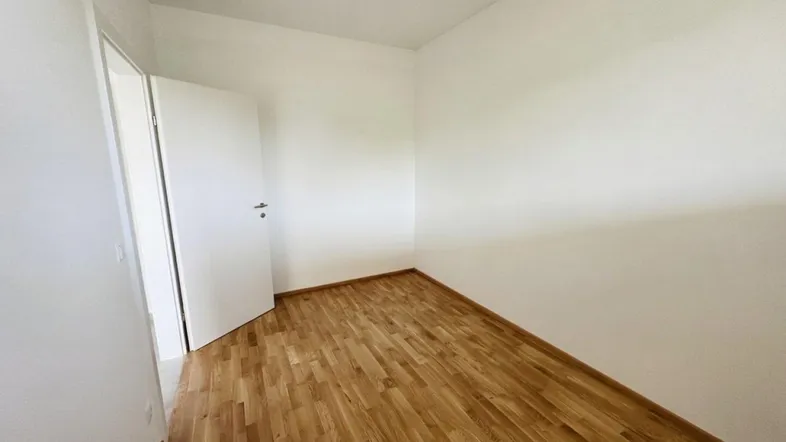 Helles, leeres Zimmer mit Holzboden und weißen Wänden, bereit zur individuellen Gestaltung.