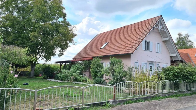 Einfamilienhaus mit großem Garten, überdachter Terrasse und gepflegter Außenanlage unter bewölktem Himmel.