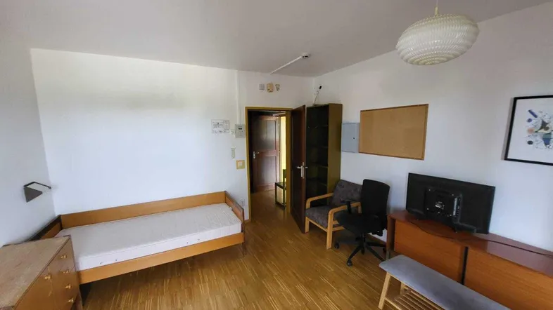 Helles Schlafzimmer mit Einzelbett, Schreibtisch und Holzparkettboden, ideal für Studenten oder Gäste.