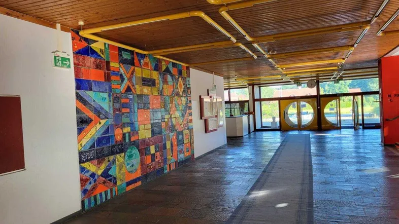 Geräumiger Flur mit farbenfroher Wandkunst, Holzbalkendecke und großen Fenstern zum Außenbereich.