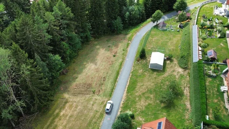 Luftaufnahme eines weitläufigen Grundstücks mit angrenzendem Wald und Zufahrtsstraße.