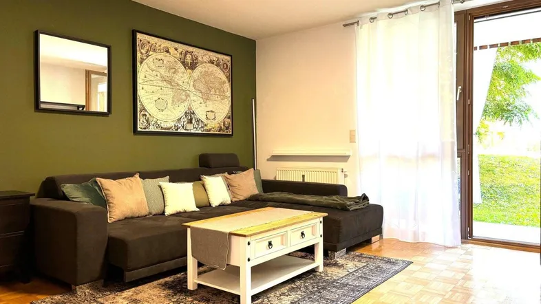 Gemütliches Wohnzimmer mit dunkelgrüner Akzentwand, Parkettboden und Zugang zum Balkon.