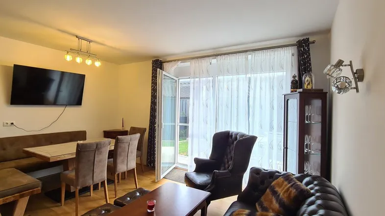 Gemütlicher Wohn-Essbereich mit dunklem Ledersofa, Esstisch und Zugang zum Garten.