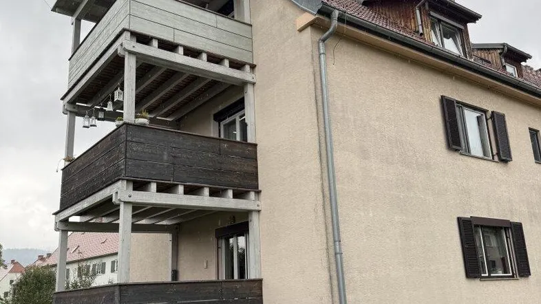 Mehrstöckiges Wohngebäude mit gestapelten Holzbalkonen und Satteldach in grüner Umgebung.