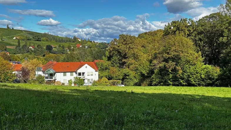 Weitläufige Landschaft mit einem Wohnhaus, umgeben von grünen Hügeln und Weinbergen unter blauem Himmel.
