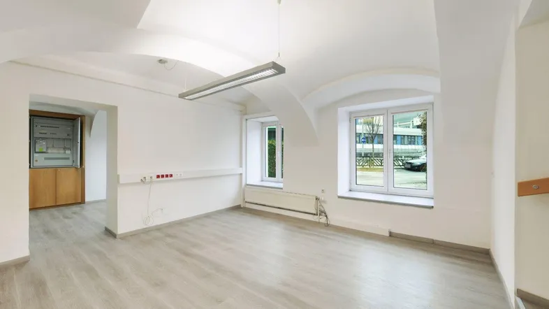 Heller, leerer Raum mit Gewölbedecke, großen Fenstern und modernem Laminatboden, ideal für Büronutzung.