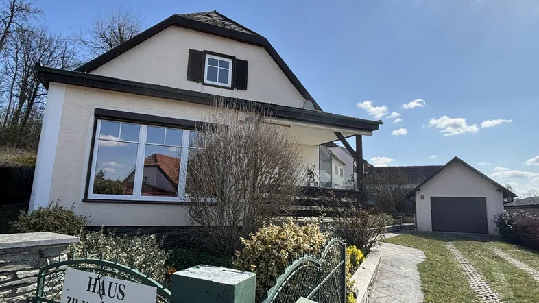Charmantes Einfamilienhaus mit Vorgarten, separater Garage und sonnigem Himmel.