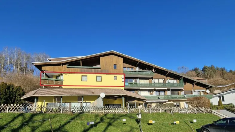 Mehrfamilienhaus mit gelber Fassade und mehreren Balkonen in sonniger Hanglage.