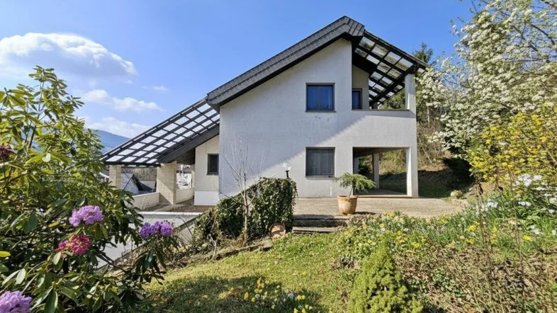 Modernes Einfamilienhaus mit weißer Fassade, Satteldach und gepflegtem Vorgarten in sonniger Hanglage.