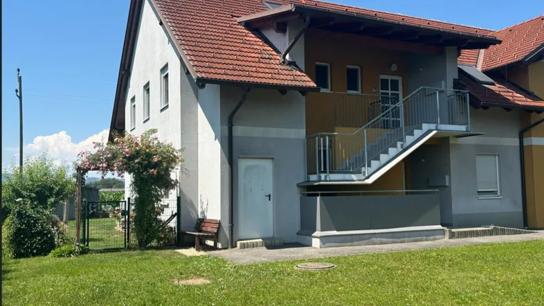 Mehrfamilienhaus mit Satteldach, Außentreppe und gepflegtem Rasen in ländlicher Umgebung.