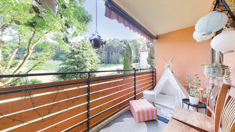Gemütlicher Balkon mit Holzzaun, Markise und weitem Blick ins Grüne.
