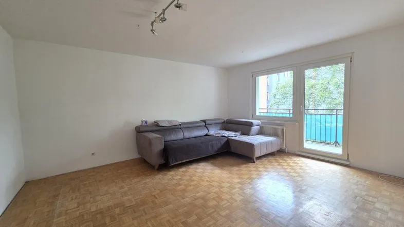 Helles Wohnzimmer mit Parkettboden und Zugang zu einem kleinen Balkon, ideal zum Entspannen.