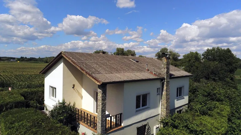 Luftaufnahme eines Hauses mit Balkon und Blick auf umliegende Felder unter blauem Himmel.