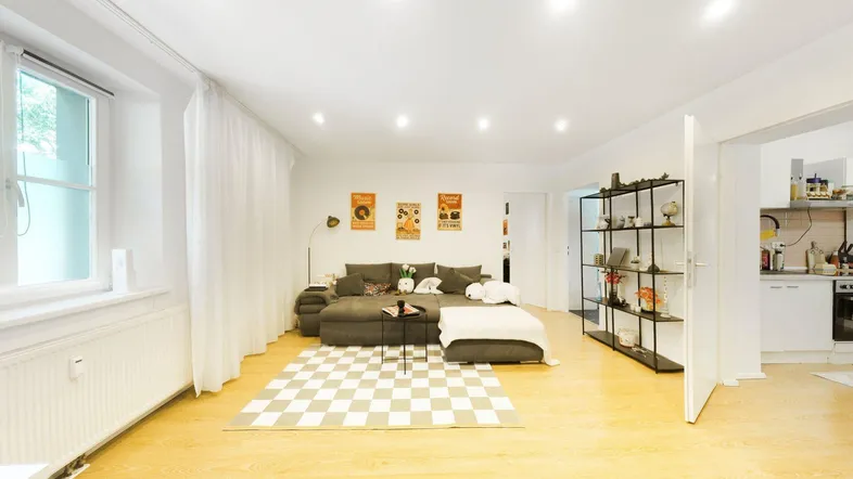 Helles Wohnzimmer mit großem Sofa, Parkettboden und Blick in die angrenzende Küche.