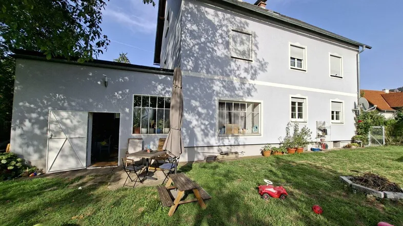 Hinteransicht des Hauses mit großem Garten, Außensitzbereich und Kinderspielzeug auf der Wiese.