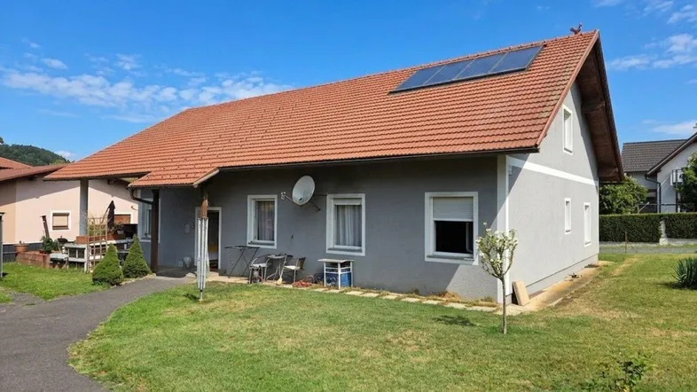 Einfamilienhaus mit Satteldach, Photovoltaikanlage und gepflegtem Vorgarten unter blauem Himmel.