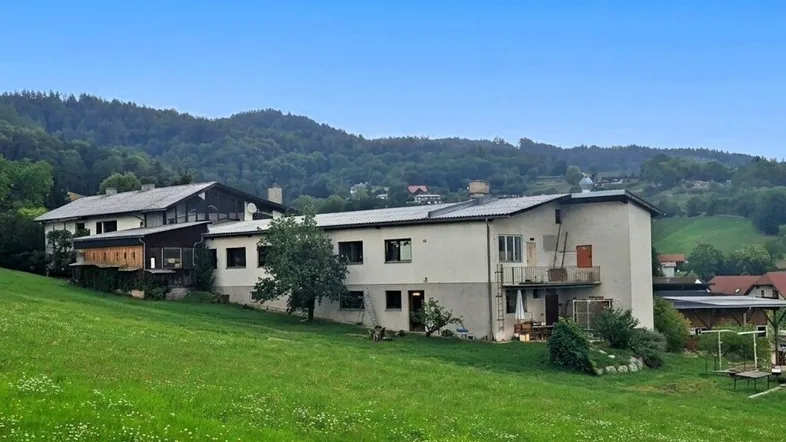 Gebäude in ländlicher Umgebung mit grünen Hügeln und Bäumen im Hintergrund.