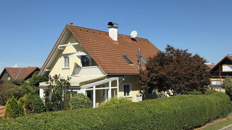 Gelbes Einfamilienhaus mit rotem Ziegeldach und gepflegter Hecke im Vorgarten.