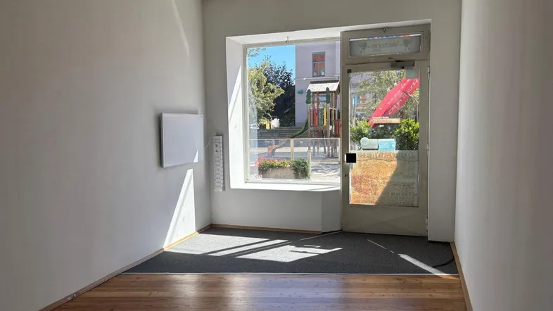 Heller, leerer Raum mit großen Fenstern und Holzboden, ideal für ein Geschäft oder Büro.