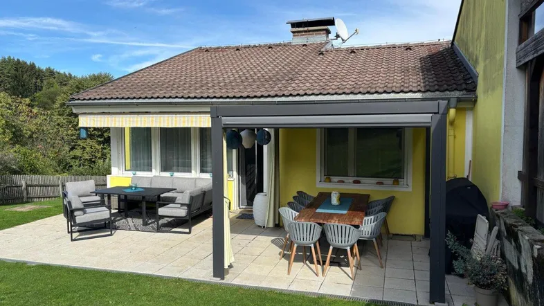 Große gepflasterte Terrasse mit zwei Sitzbereichen und Markise, ideal für Entspannung im Freien.