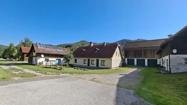 Ländliches Anwesen mit mehreren Gebäuden, umgeben von grüner Natur und Bergen.