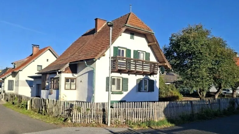 Traditionelles Einfamilienhaus mit Satteldach, Balkon und Holzzaun unter blauem Himmel.
