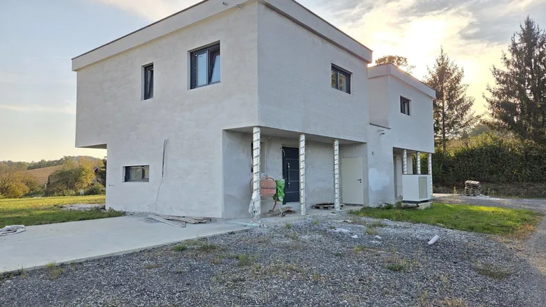 Modernes Einfamilienhaus im Bau mit heller Fassade und Flachdach unter einem Abendhimmel.