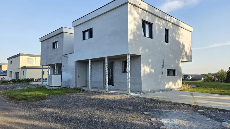 Modernes Neubauhaus mit heller Fassade und unfertiger Außenanlage bei Sonnenlicht.