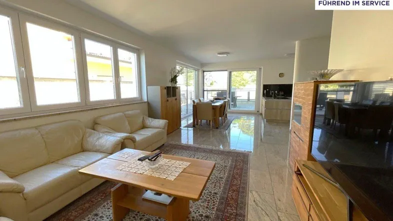 Geräumiger offener Wohn- und Essbereich mit Fliesenboden, beigen Sofas und Zugang zur Terrasse.