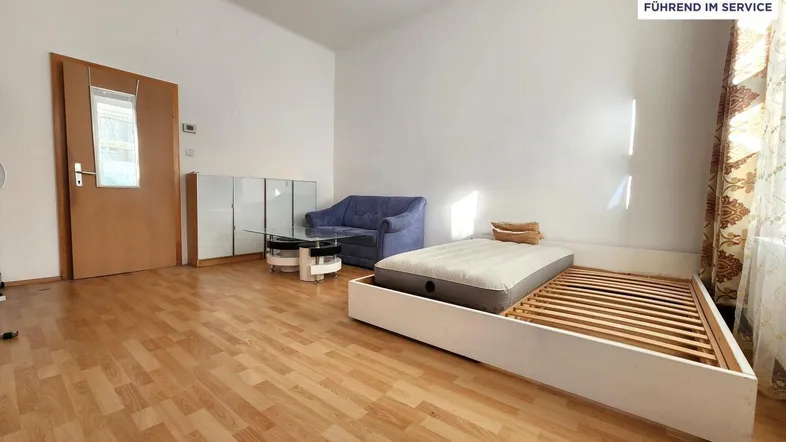 Helles Zimmer mit Laminatboden, einem Bett und einem kleinen Sofa, ideal als Wohn- und Schlafbereich.