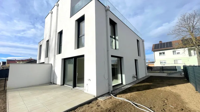 Moderne Neubau-Doppelhaushälfte mit großer Terrasse und angrenzendem Gartenbereich unter blauem Himmel.