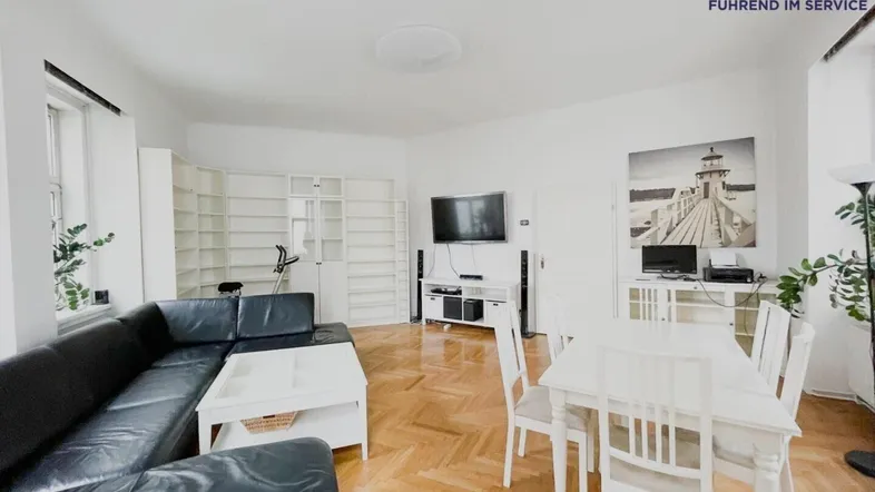 Geräumiger Wohn-Essbereich mit Fischgrätparkett, schwarzem Sofa und weißem Esstisch.