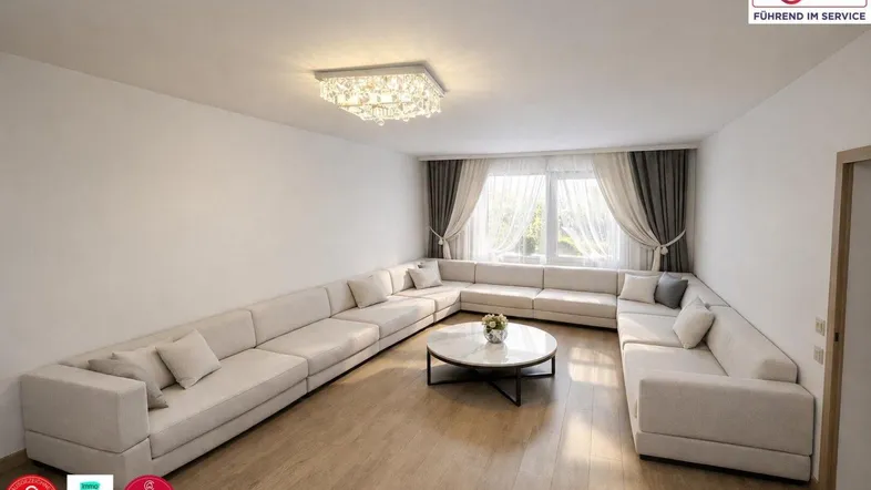 Helles Wohnzimmer mit großem Ecksofa, modernem Couchtisch und Vorhängen am Fenster.