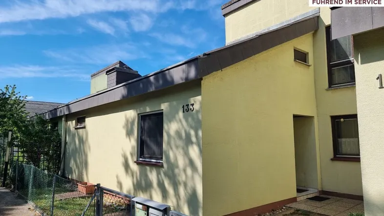 Gelbe Fassade eines Reihenhauses unter blauem Himmel mit der Hausnummer 133.