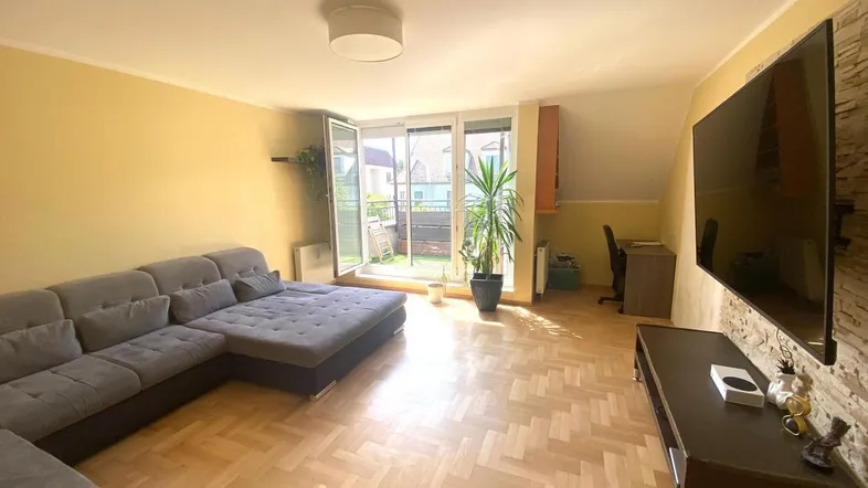 Helles Wohnzimmer mit großem Sofa, Parkettboden und Zugang zum Balkon, ideal zum Entspannen.