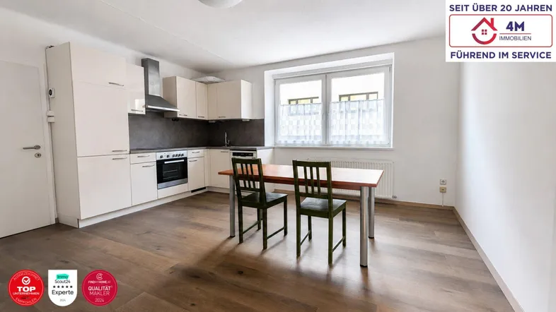 Helle, offene Küche mit weißen Schränken, Holzboden und Essbereich am Fenster.