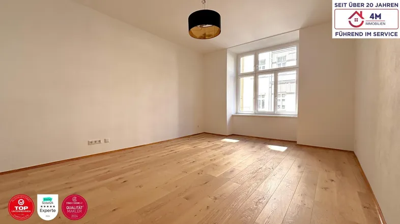 Helles Zimmer mit Holzboden und großem Fenster, ideal als Wohn- oder Schlafbereich nutzbar.