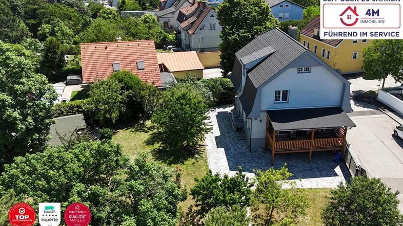 Luftaufnahme eines Einfamilienhauses mit Garten und umliegender Wohnbebauung unter blauem Himmel.