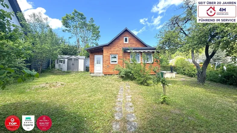 Kleines Holzhaus mit gepflegtem Garten und sonnigem Rasenbereich unter blauem Himmel.