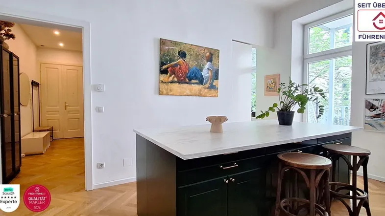 Moderne offene Küche mit Kochinsel, weißen Arbeitsplatten und Blick in den hellen Flur.