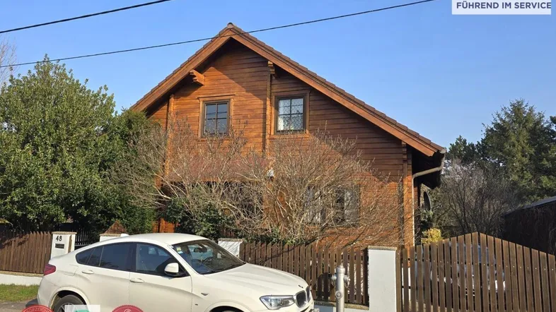 Traditionelles Holzhaus mit Satteldach und Vorgarten, umgeben von einem Holzzaun.