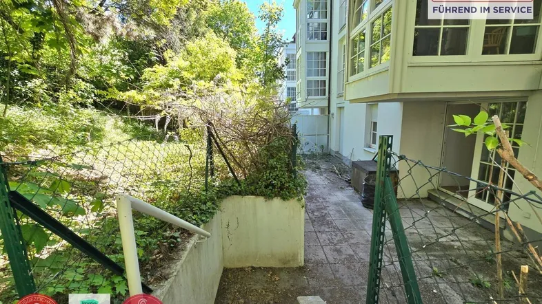 Gartenbereich mit Treppe und Zugang zum Gebäude, umgeben von viel Grün und Bäumen.