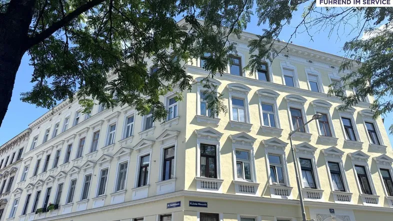 Mehrstöckiges Wohngebäude mit klassischer Architektur und vielen Fenstern in einer städtischen Umgebung.