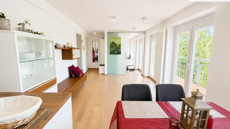 Helles Wohn- und Esszimmer mit Holzboden, Zugang zum Balkon und Blick ins Grüne.