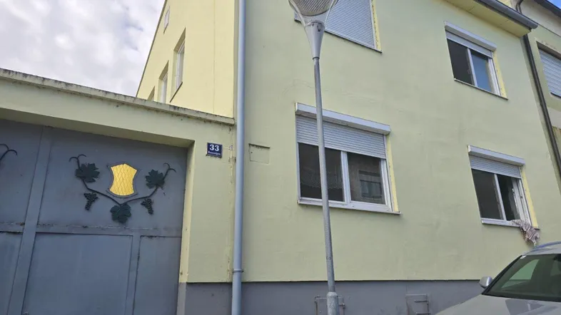 Fassade eines Wohnhauses mit gelber Putzfassade, Rollläden an den Fenstern und einer Hausnummer 33.