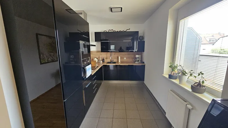 Moderne Küche mit schwarzen Hochglanzfronten, Holzarbeitsplatte und Fliesenboden, gut beleuchtet durch ein Fenster.
