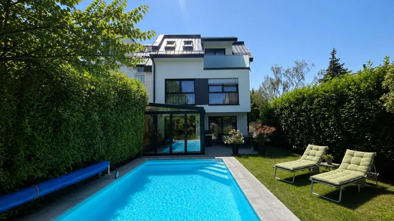 Großzügiger Gartenbereich mit privatem Pool, Liegestühlen und gepflegter Hecke unter strahlendem Himmel.